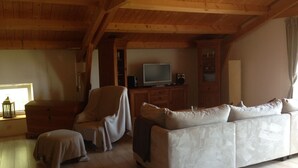 A cozy living room with a wooden ceiling, a white sofa, a chair, and a television on a wooden cabinet. - Landhaus Chlosta (Biendorf)
