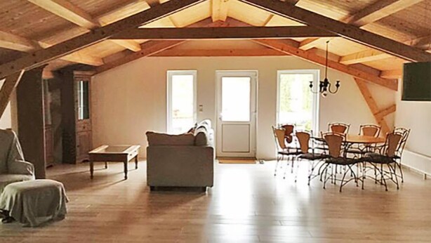 An attic room with a high ceiling, wooden beams, a sofa, a dining table with chairs, and a small table. - Landhaus Chlosta (Biendorf)