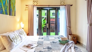 A bedroom with a bed, a bedside lamp, a window with curtains, and a view of the outside. - VILLA RETRO 88 - Short Walk to Beach - Top Located (Seminyak)