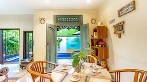 A dining area with a round table set for four, wooden chairs, and a view of a pool through an open door. - VILLA RETRO 88 - Short Walk to Beach - Top Located (Seminyak)