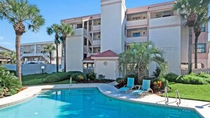 Um hotel com piscina, palmeiras e um edifício de vários andares.