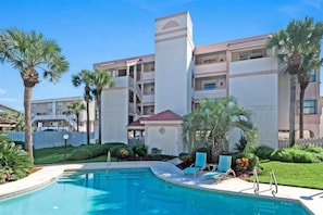 A hotel with a swimming pool, palm trees, and a multi-story building. - SeeRay Shores 102 (St. Augustine)
