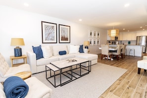 A modern living room with a white sofa, a coffee table, and a dining area with a white table and chairs.