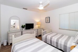 A bedroom with two beds, a dresser, a television, a ceiling fan, and a window with blinds. - SeeRay Shores 102 (St. Augustine)