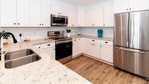 Cozinha moderna com armários brancos, eletrodomésticos de aço inoxidável e bancada de granito.