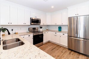 A modern kitchen with white cabinets, stainless steel appliances, and a granite countertop. - SeeRay Shores 102 (St. Augustine)