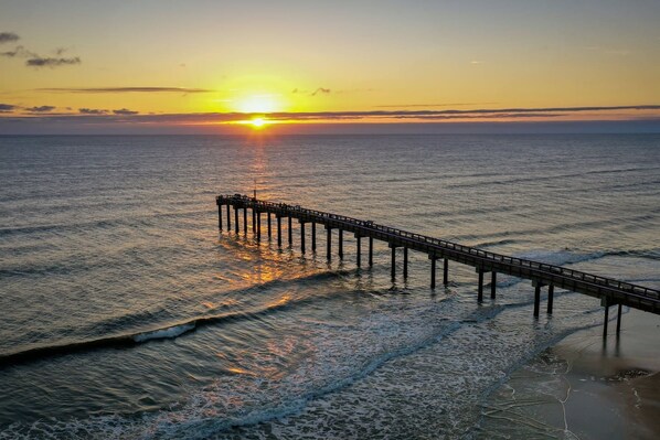Un muelle se adentra en aguas tranquilas, con un atardecer de fondo.