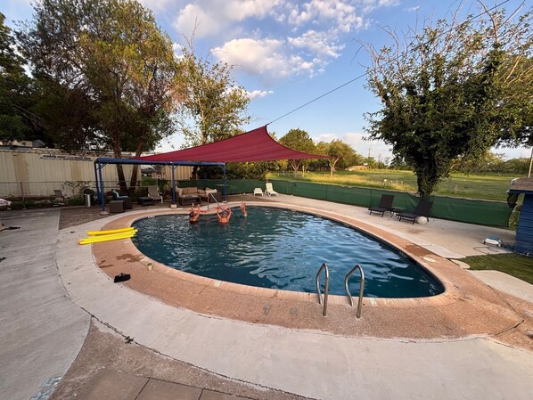 An outdoor swimming pool with a red canopy, surrounded by lounge chairs and a covered seating area.