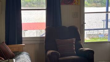 A room with a view of a lake, a chair, a couch, and a painting on the wall.