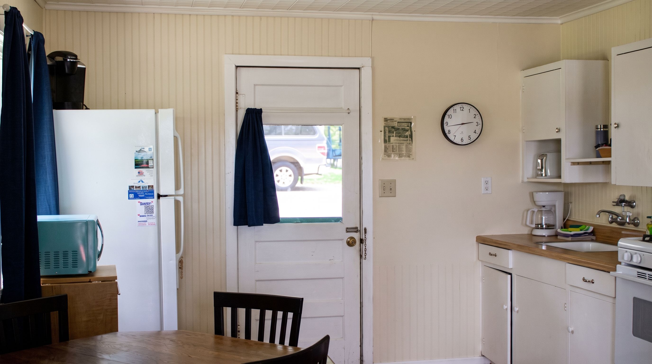 A compact kitchen with a refrigerator, a coffee maker, and a clock on the wall.