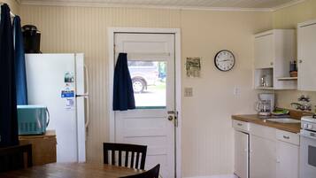 A compact kitchen with a refrigerator, a coffee maker, and a clock on the wall.