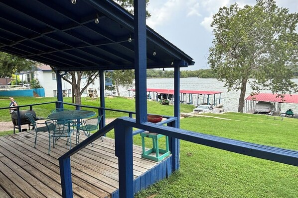 Une terrasse avec coin salon extérieur, un barbecue et une vue sur un lac où l’on peut voir des bateaux, ainsi qu’un espace abrité.