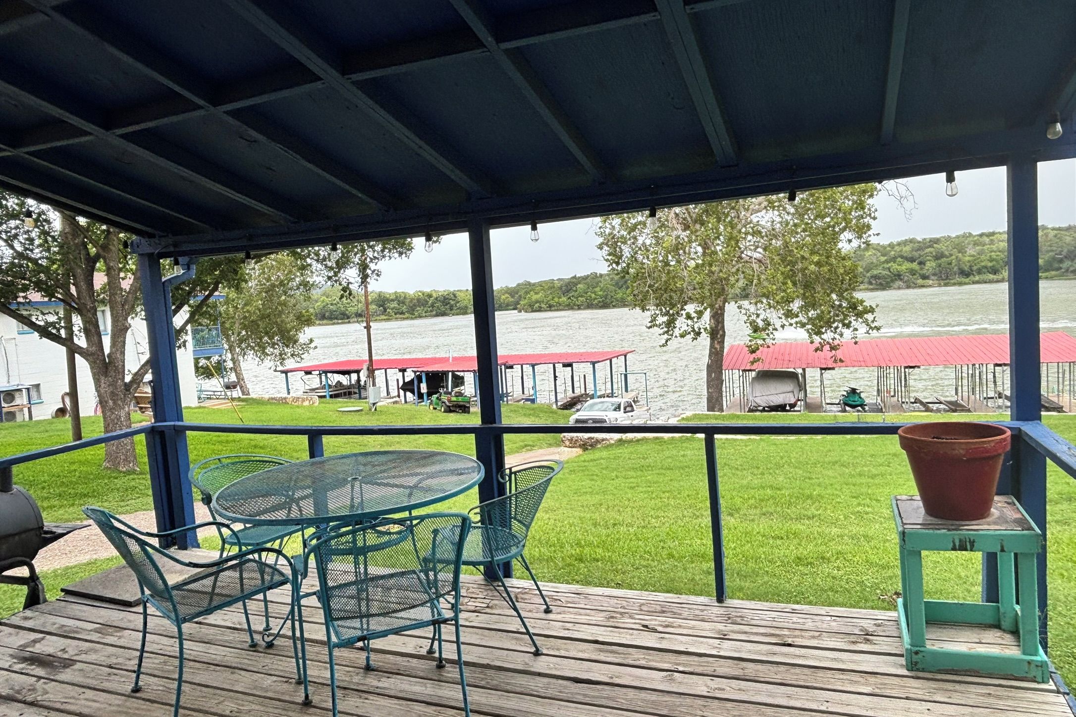 Un espace extérieur abrité, doté d’une table et de chaises, qui offre une vue sur un plan d’eau où l’on peut apercevoir des bateaux et un quai.