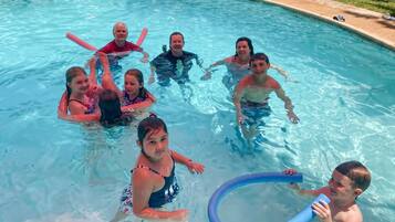Una piscina con gente en el agua, una silla de descanso y una zona de borde de piscina con escalones.