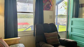 A room with a large window, a chair with a striped pillow, and a painting on the wall.