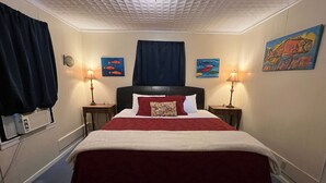 Une chambre d’hôtel comprenant un lit, deux tables de chevet, une tête de lit, une fenêtre avec des rideaux et des œuvres d’art murales.