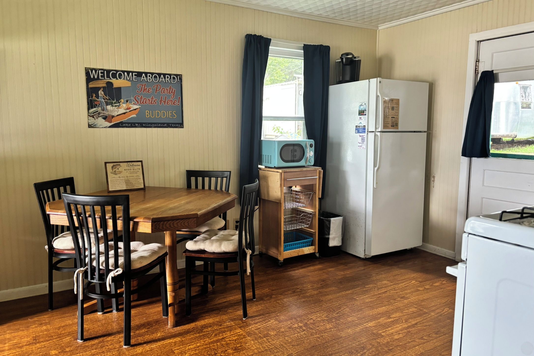 Une cuisine compacte comprenant une table à manger, des chaises, un réfrigérateur, un four à micro-ondes et une fenêtre avec des rideaux.