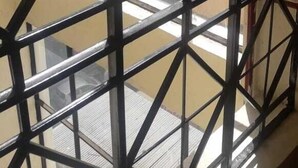 A window with a metal grid, overlooking a cityscape with buildings. - Royal Palm Hotel And Suites (Nakuru)