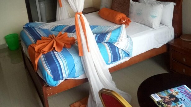 A bed with a canopy, striped bedding, and multiple pillows. - Royal Palm Hotel And Suites (Nakuru)
