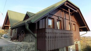A rustic wooden building with a stone foundation, a green roof, and a balcony with a decorative railing.