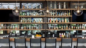 A bar with multiple shelves of liquor bottles, a fruit bowl, and bar stools. - Canopy by Hilton Austin Downtown (Austin)