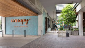 A modern building entrance with a prominent 'canopy' sign, a herringbone brick floor, and a tree in the center. - Canopy by Hilton Austin Downtown (Austin)