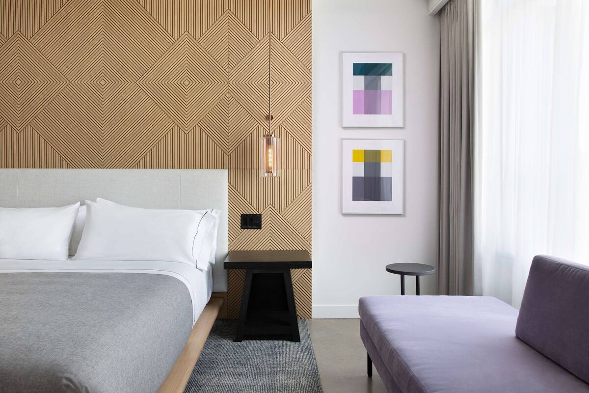 A modern hotel room with a bed, a small table, a sofa, and a patterned wall.