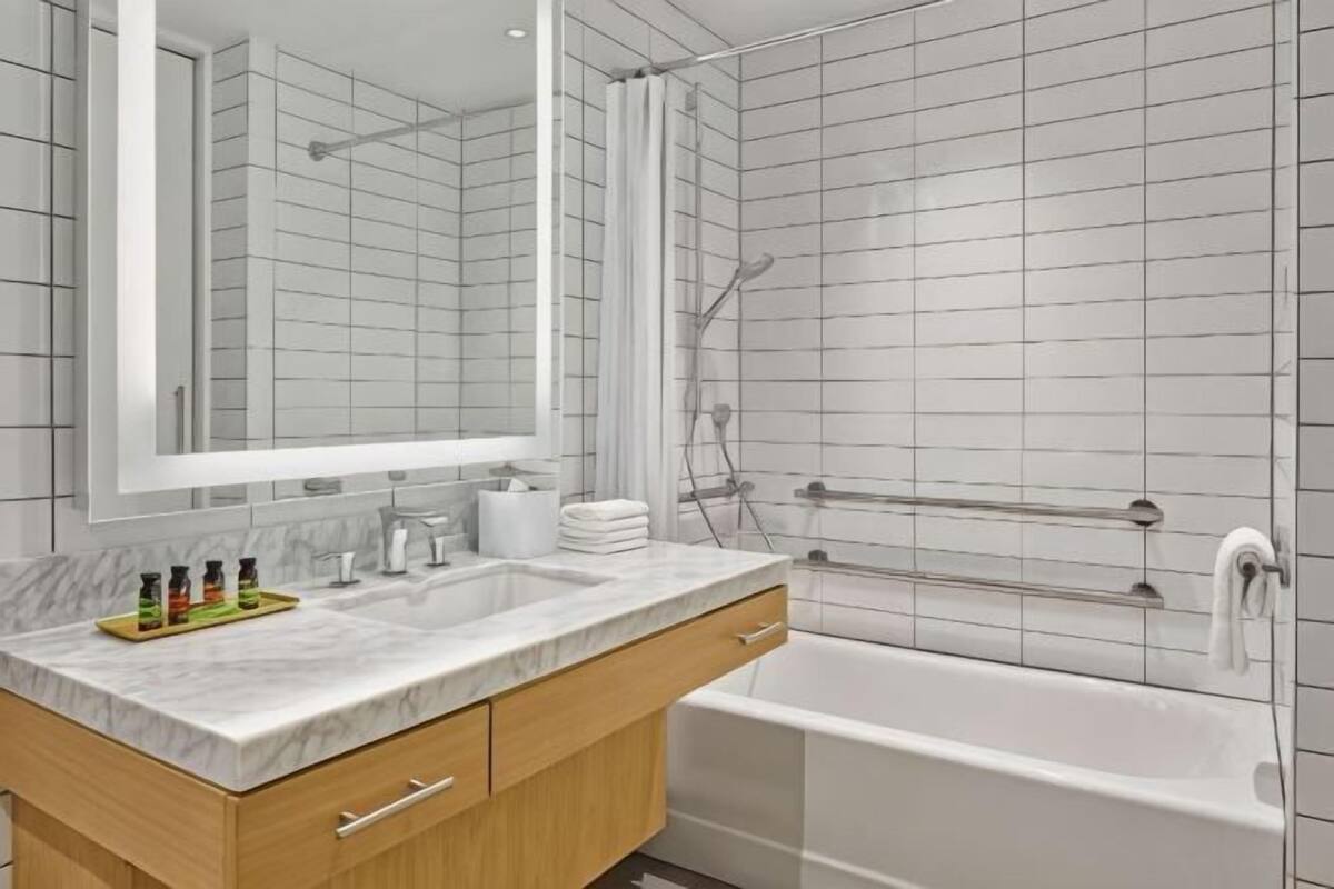 A modern bathroom with a marble sink, a large mirror, a bathtub, and a shower area.