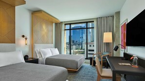 A hotel room with two beds, a desk, a chair, a TV, and a large window with a city view. - Canopy by Hilton Austin Downtown (Austin)