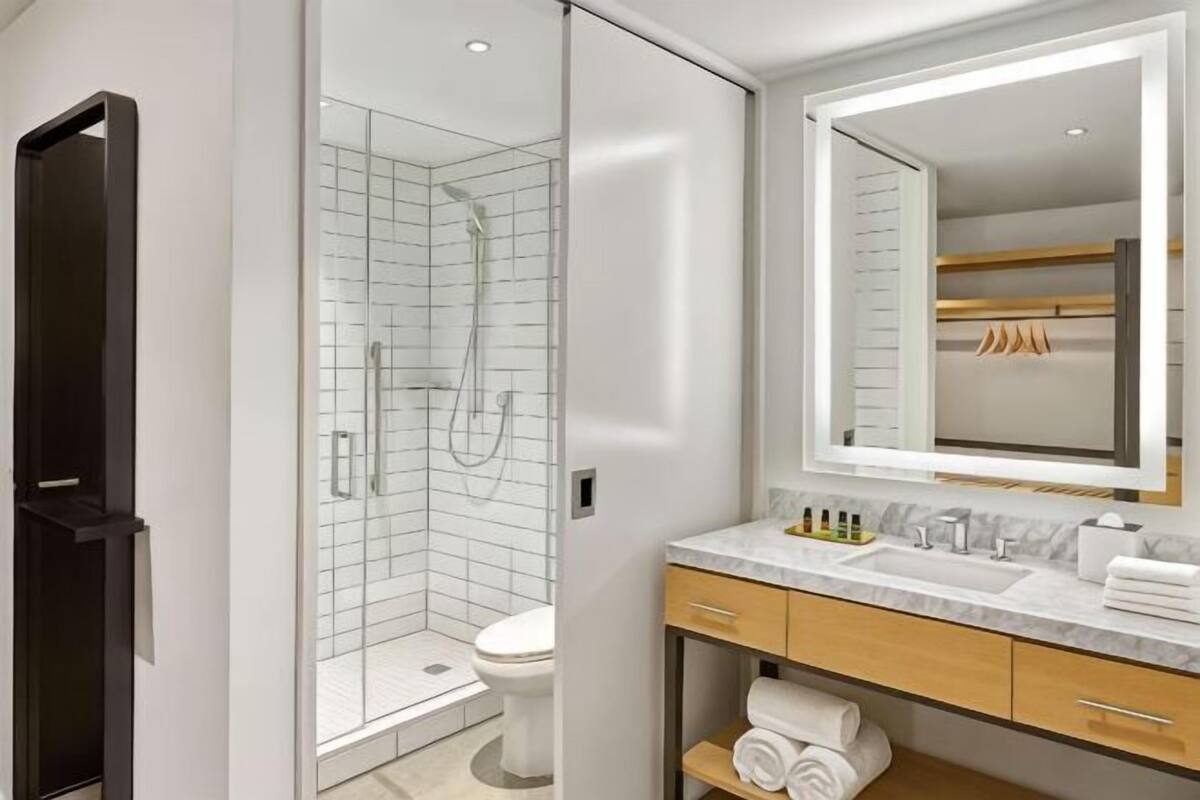 A modern bathroom with a glass shower enclosure, a toilet, a sink with a mirror, and a wooden vanity.