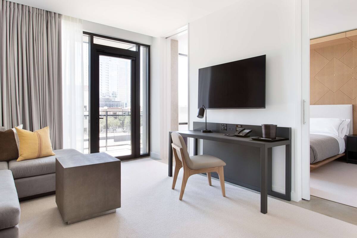 A modern hotel room with a sofa, a desk with a flat-screen TV, a chair, and a bed.