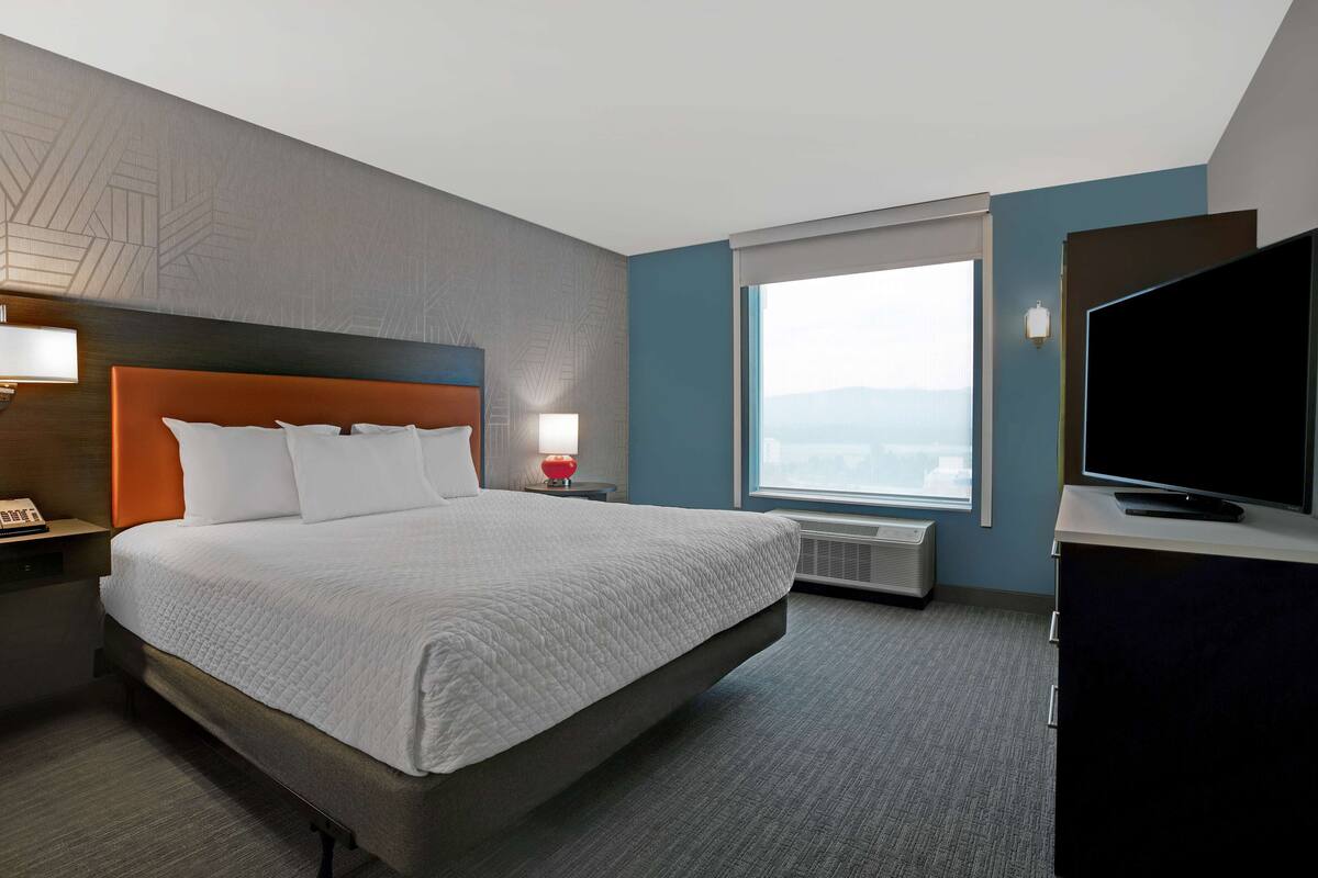 Ein Hotelzimmer mit einem großen Bett, einem Flachbildfernseher, einem Fenster mit Blick auf die Stadt und einem Wandheizkörper.