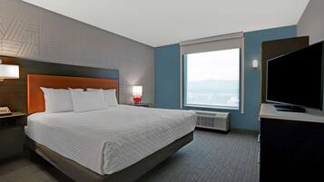 A hotel room with a large bed, a flat-screen TV, a window with a city view, and a wall-mounted heater.