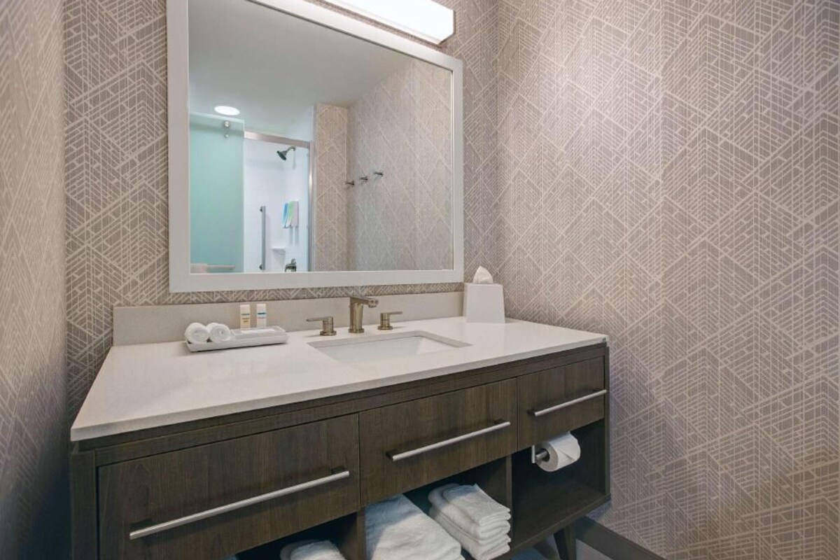 A modern bathroom with a large mirror, a sink, and a vanity with drawers and a shelf.