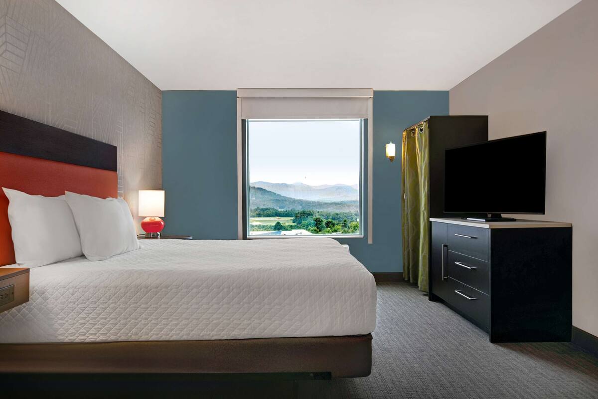 Ein Hotelzimmer mit einem großen Bett, einem Flachbildfernseher, einem Schminktisch und einem Fenster mit Bergblick.