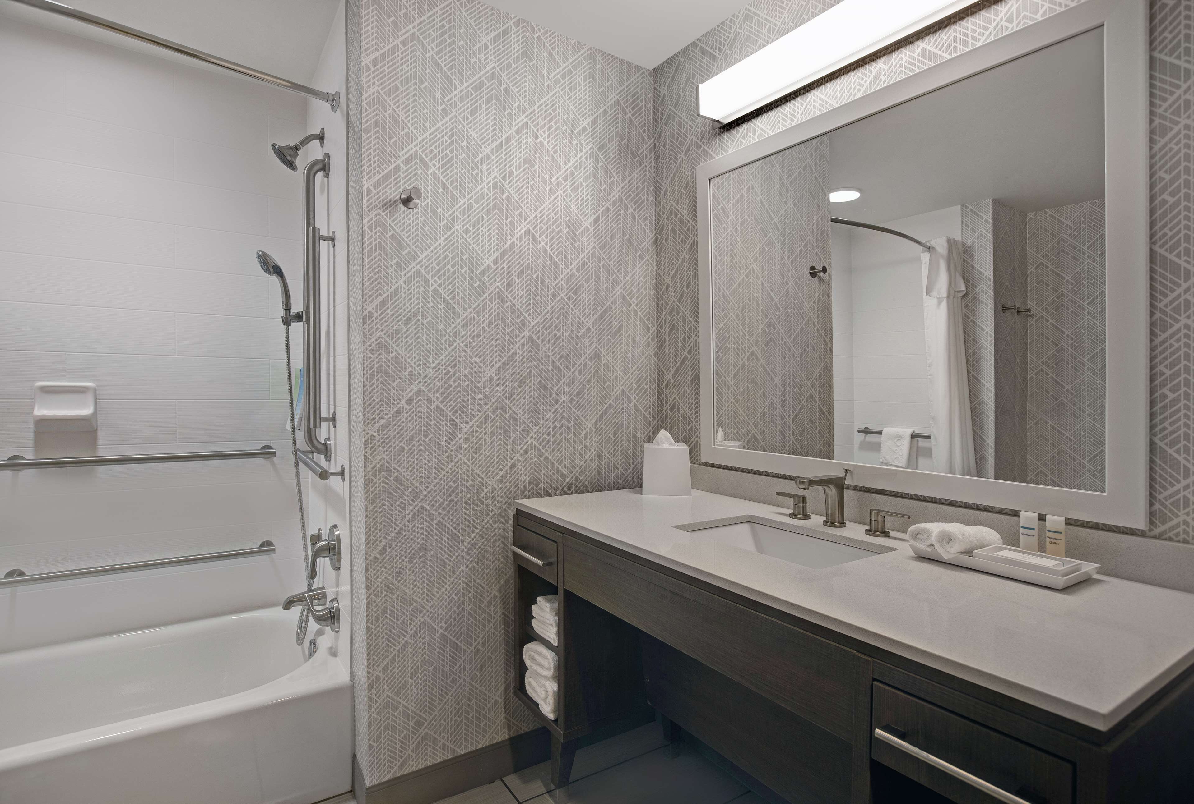 Un baño moderno con bañera, un espejo grande, un lavabo y un perchero para toallas.