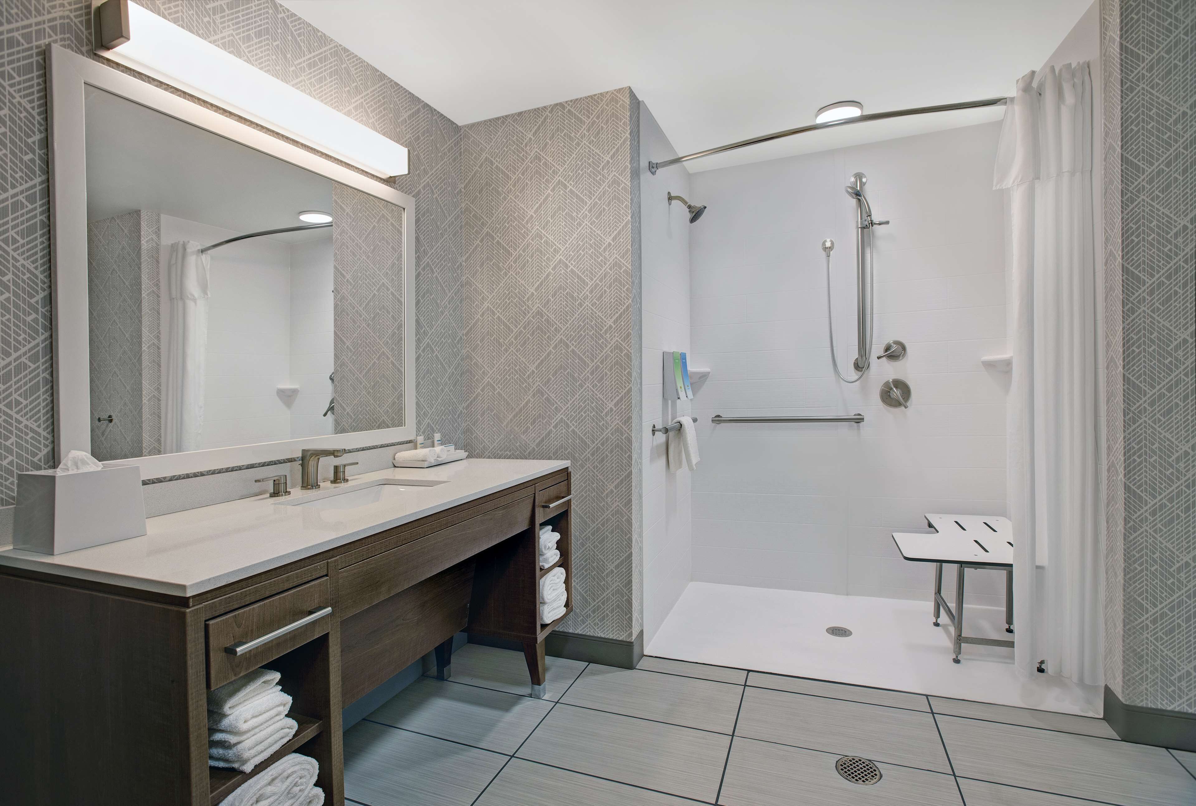 A modern bathroom with a large mirror, two sinks, a shower with a glass door, and a small table.
