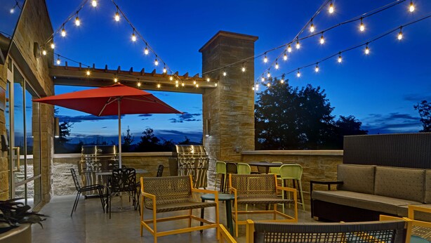 An outdoor patio area with string lights, a red umbrella, wicker furniture, and a stone pillar.