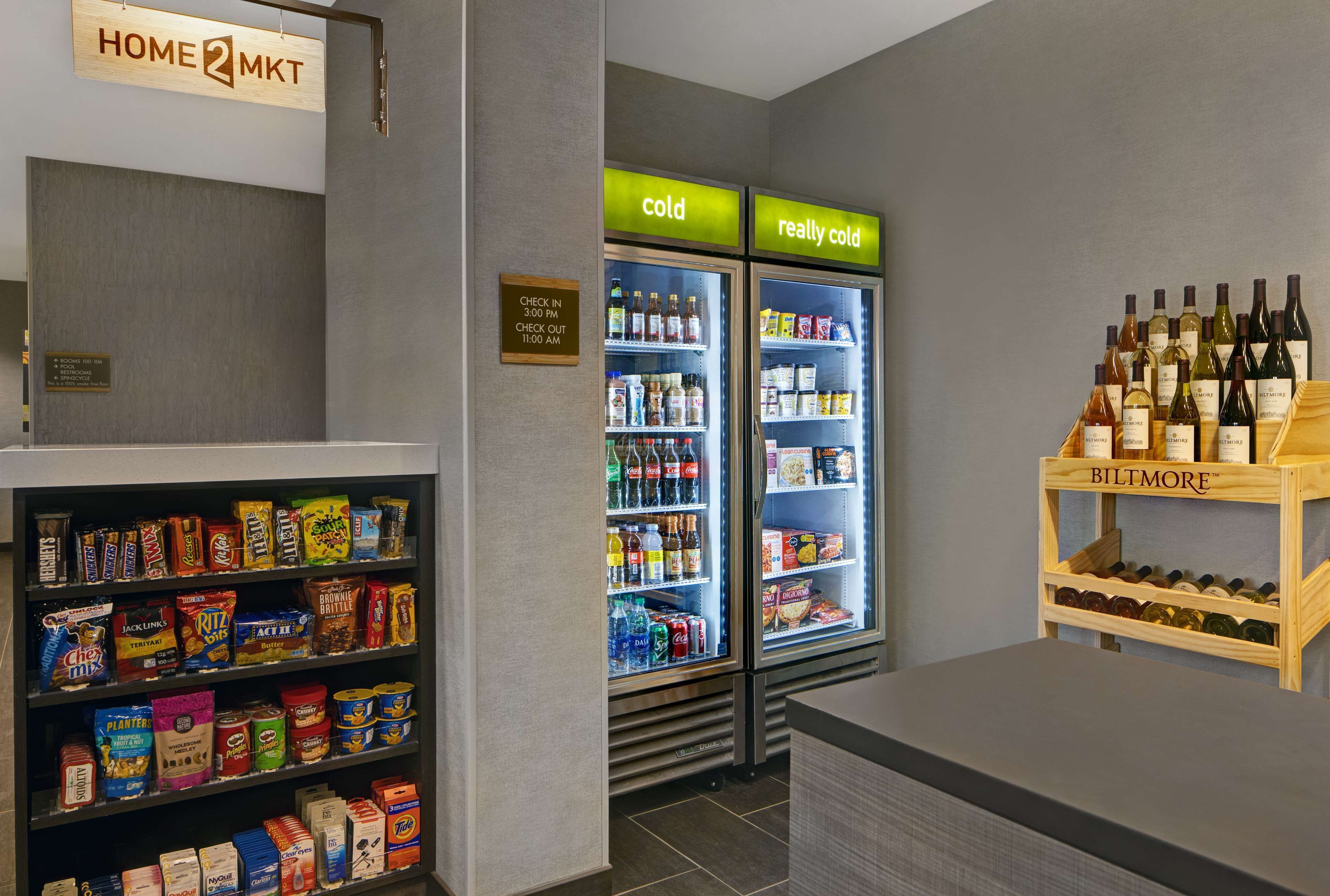 Un vestíbulo de hotel con una barra de aperitivos, dos refrigeradores para bebidas etiquetados como 'frío' y 'muy frío', y una vitrina para vinos.