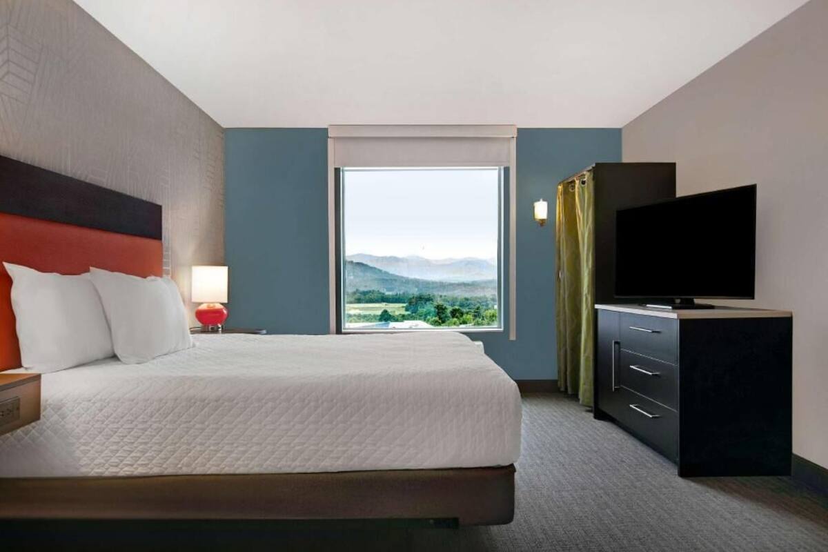 Ein Hotelzimmer mit Bett, Fernseher, Schminktisch und Fenster mit Bergblick.