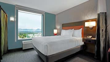 A hotel room with a large bed, a nightstand with a lamp, a phone, and a view of the city through a large window.