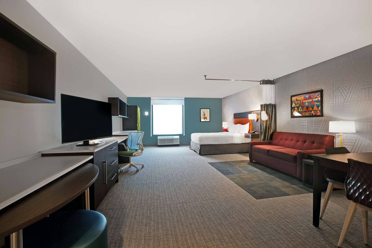Ein Hotelzimmer mit einem Bett, einem Schreibtisch, einem Sessel, einer Couch und einem Fernseher.