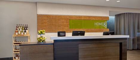 Un mostrador de recepción moderno de hotel con un panel de pared de madera, una pantalla digital y un estante para vinos.