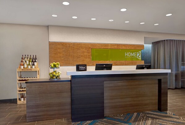 Un mostrador de recepción moderno de hotel con un panel de pared de madera, una pantalla digital y un estante para vinos.