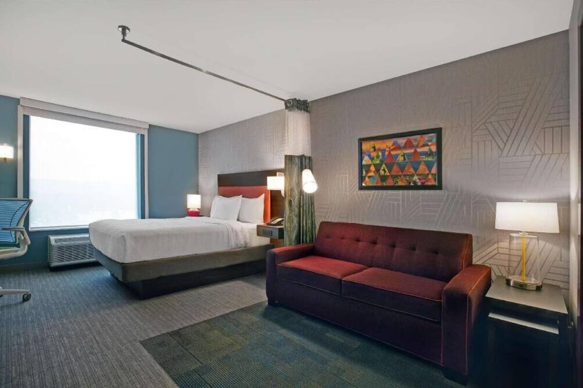 Ein Hotelzimmer mit einem Bett, einem roten Sofa, einem Schreibtisch mit einer Lampe und einem Fenster.