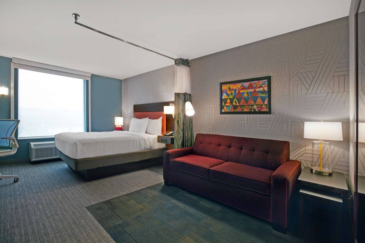 Ein Hotelzimmer mit einem Bett, einem roten Sofa, einem Schreibtisch mit Lampe und einem Bild an der Wand.