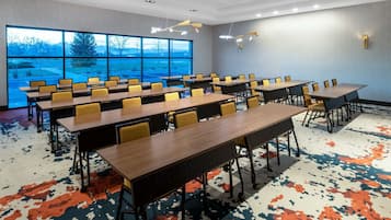 Un salón de conferencias con varias mesas y sillas, amplias ventanas que dan a vistas de árboles y montañas, y una alfombra estampada.
