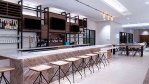 A modern bar area with a long counter, multiple stools, and shelves stocked with bottles and glasses.