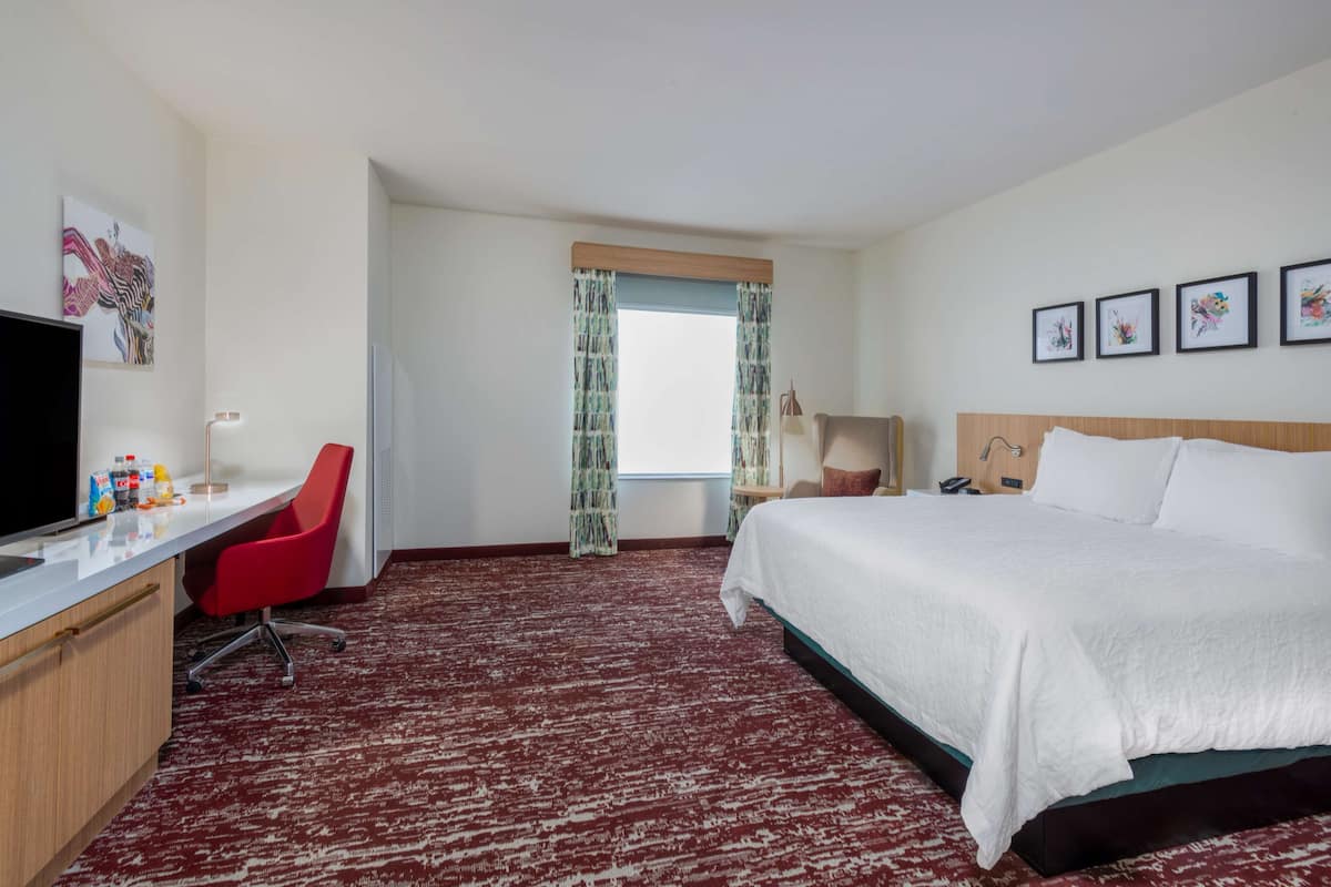 A hotel room with a bed, desk, chair, television, and artwork on the walls.