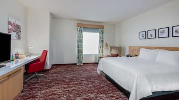 A hotel room with a bed, desk, chair, television, and artwork on the walls.